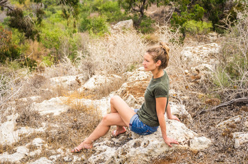 A woman sits on a stony hill and looks at a natural landscape in the distance