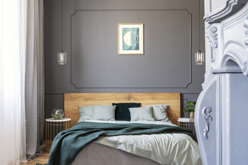 Graphic on the wall decorated with molding in a bedroom interior with a double bed with pillows and blanket