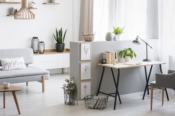 Grey armchair at desk with plant and lamp in flat interior with wooden table next to couch. Real photo