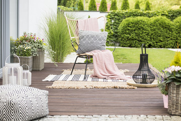 Real photo of a white pillow and pink blanket on a rattan chair standing in the garden of a...