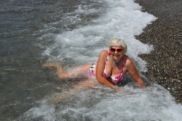 Fototapeta premium Aged lady is lying on water edge at the sea beach.