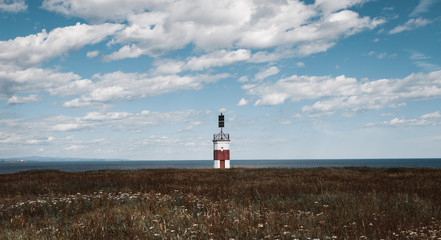 Fototapeta na wymiar A lonely red and white lighthouse in a field on the shores of the Okhotsk Sea in the north of the Khabarovsk Territory of Russia. Beautiful background