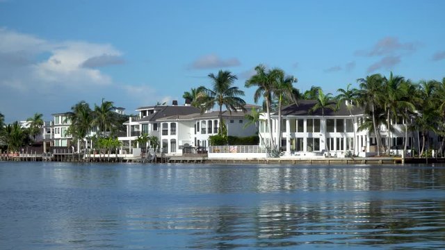 Establishing shot of generic luxury vacation mansion homes along coastal water way during beautiful summer day time. Exterior lock down view in 4K along shore line.