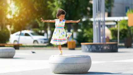A happy black child. Little African American girl dances in the city square.