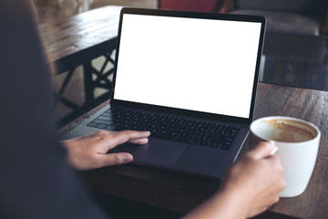 Mockup image of a woman using laptop with blank white desktop screen while drinking hot coffee on wooden table in cafe