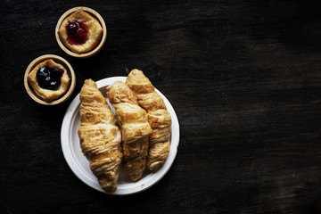 The croissant dish put beside blueberry pie in wooden cup,on wooden desk,vintage and art tone,blurry light around