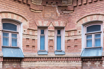 Naklejka premium Two vintage arched windows in a wall of yellow bricks. Green - the colors of sea wave glass in a maroon dark red wooden frame. The concept of antique vintage architecture in building elements