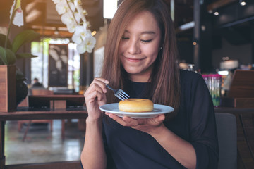 A beautiful asian woman holding a piece of donut and fork with feeling happy in cafe