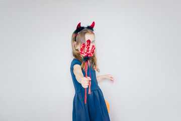cheerful happy little girl with red horns and a Trident stands on a gray background. selective focus.