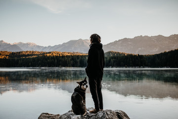 Fototapeta na wymiar Frau steht mit ihrem Hund am Ufer des Eibsee in Bayern 