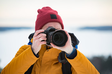Obraz premium Portrait of mature man with grey beard exploring Finland in winter. Traveler Taking pictures on the top of rock. Beautiful view of northern landscape with frozen Baltic Sea and snowy islands.