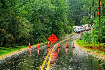 An emergency road closure on a wet paved road after storm damage with utility trucks in the...