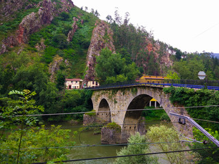 Stoned bridge crossing Nalon river between mountains, in Asturias, Spain
