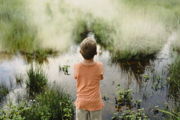 Child from behind looking at the calm water of a lake