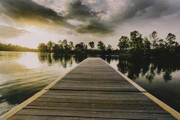 Wooden jetty over the lake at sunset in a sky with clouds
