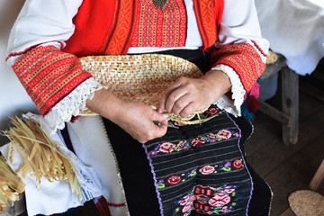 Hands of middle-aged woman osier-knitter craftswoman, dressed in Bulgarian folk costume, Etara ethnographic reserve, Bulgaria - obrazy, fototapety, plakaty