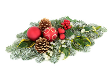 Christmas and winter table decoration with bauble decorations, holly berries, snow covered spruce pine, mistletoe, ivy and pine cones on white background.