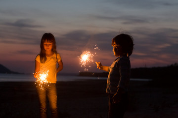happy smiling children with Sparklers on the beach at night.