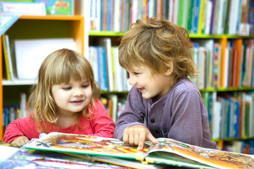 Cute two little kids, brother and sister  reading a book together in library