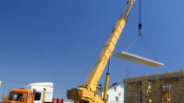 The mobile crane moves the concrete slab to the building.
