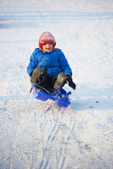 Fototapeta na wymiar Child boy jumping on bobsled. Having fun on the snow. Children winter activities.