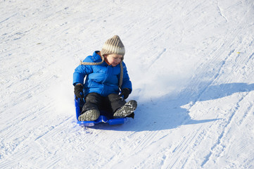 Child boy riding a bobsled. Having fun on the snow. Children winter activities.