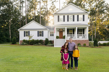 Family of Four With Daughters Outside Their New Construction White Farmhouse Home