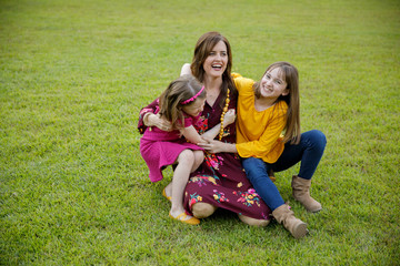 Naklejka na ściany i meble Mom and Two Daughters Laying on Ground Grass Wrestling Being Silly Having Fun Laughing