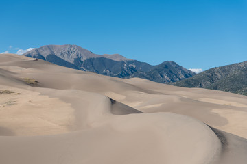 Fototapeta na wymiar Vast landscape of dunes curving towards the Rocky Mountains in Great Sand Dunes National Park, Colorado