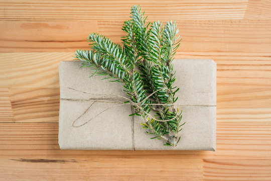 Present for Christmas wrapped in natural organic recycled paper with pine branches on wooden background. © cronislaw