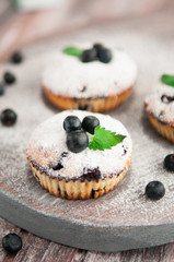 Blueberry muffins which are decorated with powdered sugar, blueberries and mint. Photo in a rustic style on a wooden background. Blurred.