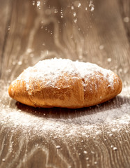 Tasty croissant powdered with sugar on wooden table