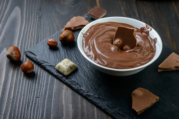 Chocolate cream in a bowl, nuts  and chocolate pieces on dark table.