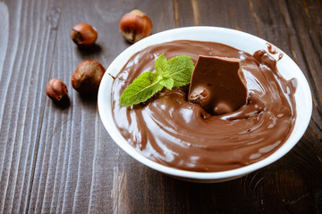 Chocolate cream in a bowl, nuts  and chocolate pieces on dark table.