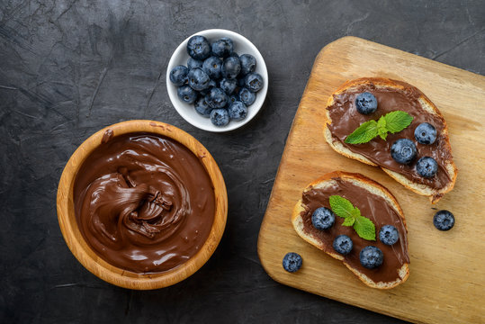 Bread with chocolate cream, blueberry  and hazelnuts on dark background