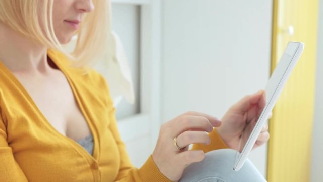 Portrait of attractive blonde Caucasian woman smiling and using digital tablet.