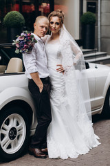 A newlyweds trip in the car. The groom invites the bride in a white cabriolet.