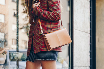 street style, attractive woman wearing a  mini skirt, check plaid blazer and a lether brown tote...