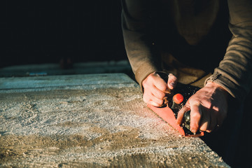 Man woodworker carpenter working with a hand plane. Planing a board is flying shavings. Master manual labor.
