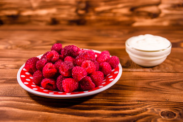 Ceramic plate with ripe raspberries and sour cream on wooden table