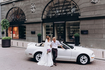A newlyweds trip in the car. The groom invites the bride in a white cabriolet.