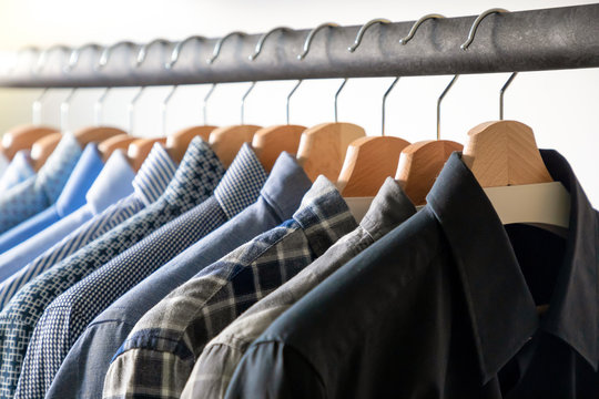 Row of men's shirts in blue colors on hanger on white background