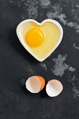 Raw egg broken in a bowl and eggshell on a dark concrete background. Flat lay