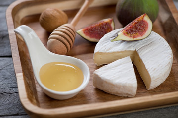 Close-up of a brown wooden serving tray with camembert cheese, honey and fig fruits, selective focus