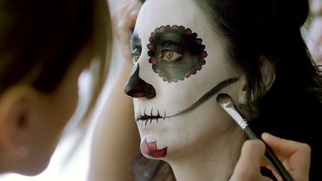 Halloween face art. Make-up artist is making woman up as skeleton for celebration of the Mexican Day of the Dead. 4K