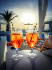 Two glasses with Aperol Spritz (aperitif cocktail consisting of prosecco, Aperol and soda water) near a swimming pool at sunset