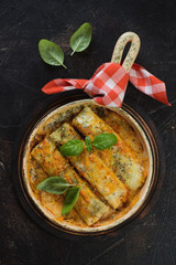 Above view of cannelloni with spinach and cheese filling in a baking dish, vertical shot on a dark brown stone background