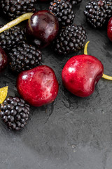 Delicious and appetizing fruits of the forest, blackberries and fresh and raw cherries. On dark background.