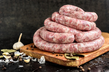 Homemade raw pork sausage on wooden cutting board on black background with garlic and spices.