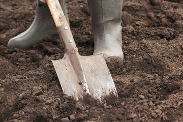 A man in boots digs the earth with a shovel